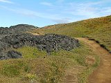 The path down eventually reaches soil and grass among the piles of dried lava.